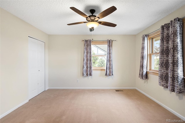 empty room featuring light colored carpet, ceiling fan, a textured ceiling, and baseboards