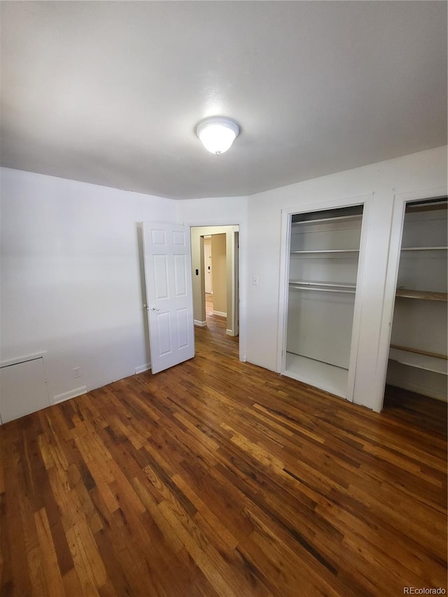 unfurnished bedroom featuring dark wood-type flooring and two closets