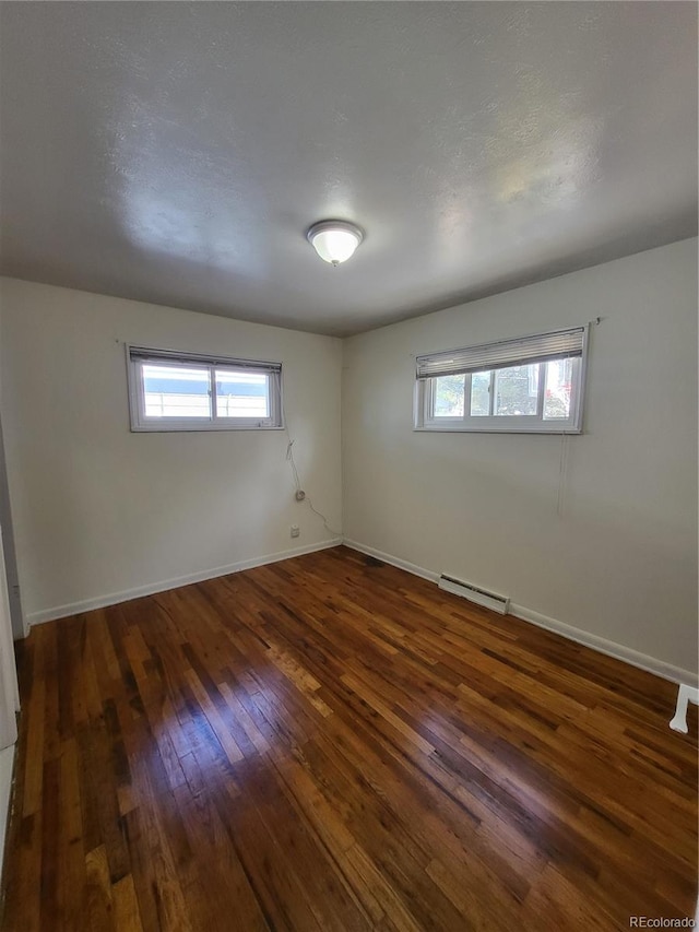 spare room with a healthy amount of sunlight, baseboard heating, and dark hardwood / wood-style floors