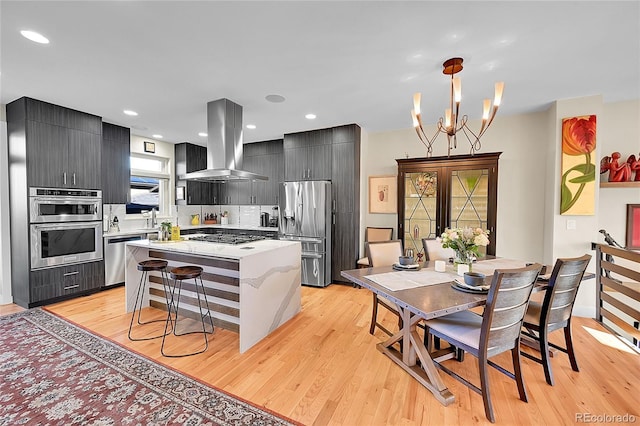 kitchen featuring appliances with stainless steel finishes, island range hood, pendant lighting, a center island, and light hardwood / wood-style floors