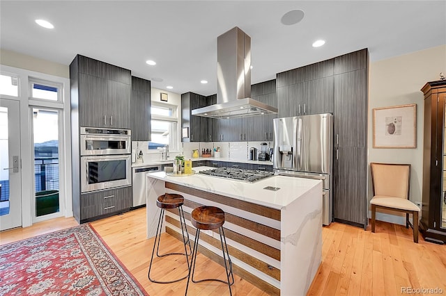 kitchen featuring island range hood, a center island, light wood-type flooring, appliances with stainless steel finishes, and a kitchen breakfast bar