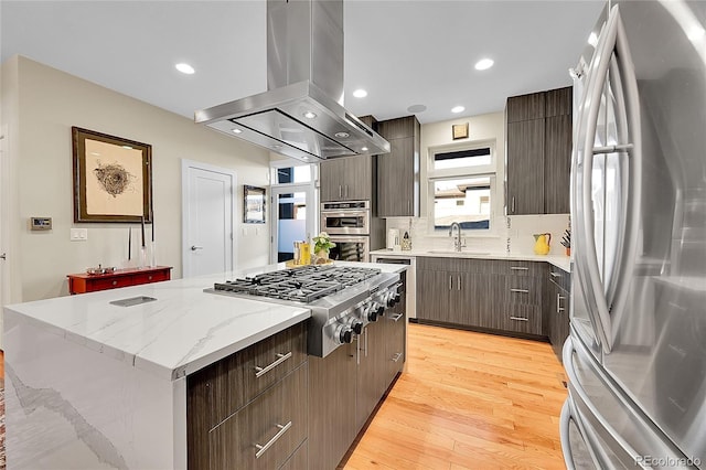 kitchen with a kitchen island, appliances with stainless steel finishes, sink, island exhaust hood, and light hardwood / wood-style floors