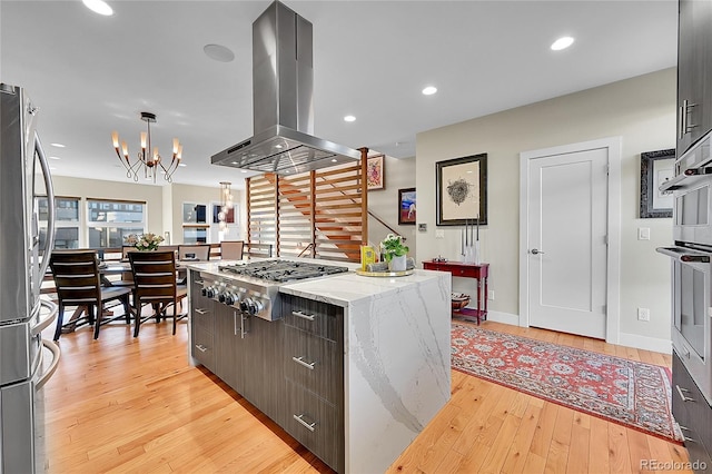 kitchen featuring a chandelier, hanging light fixtures, light hardwood / wood-style flooring, island exhaust hood, and stainless steel appliances