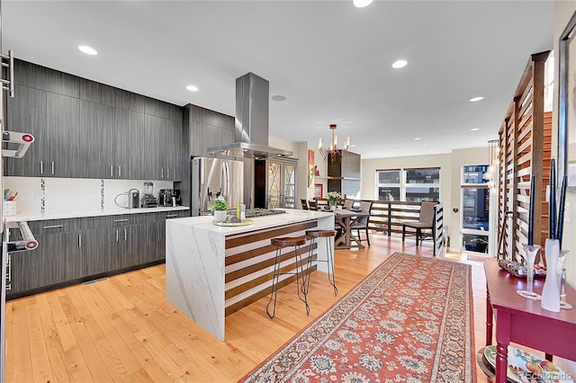 kitchen featuring island range hood, decorative light fixtures, a center island, stainless steel refrigerator with ice dispenser, and light wood-type flooring