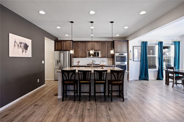 kitchen with hardwood / wood-style flooring, appliances with stainless steel finishes, backsplash, a kitchen island with sink, and hanging light fixtures