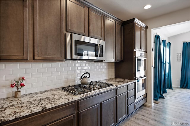 kitchen featuring dark brown cabinetry, stainless steel appliances, decorative backsplash, light stone counters, and light hardwood / wood-style flooring