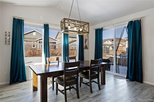 dining space with vaulted ceiling, a wealth of natural light, an inviting chandelier, and hardwood / wood-style floors