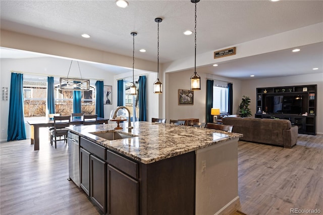 kitchen with dark brown cabinets, light stone countertops, pendant lighting, stainless steel dishwasher, and sink