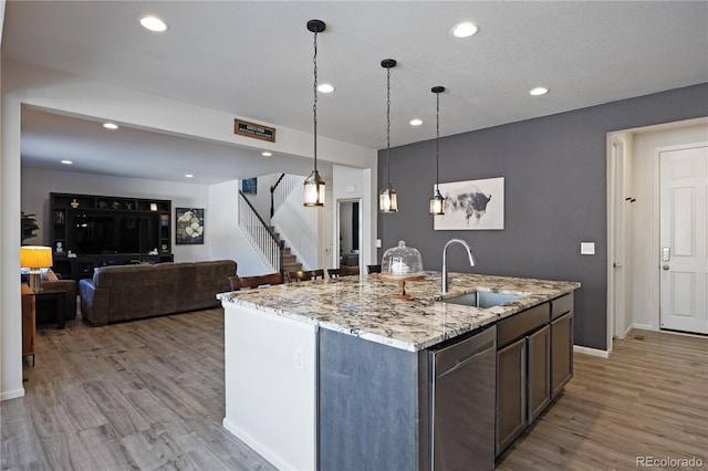 kitchen featuring pendant lighting, stainless steel dishwasher, sink, a kitchen island with sink, and light stone counters