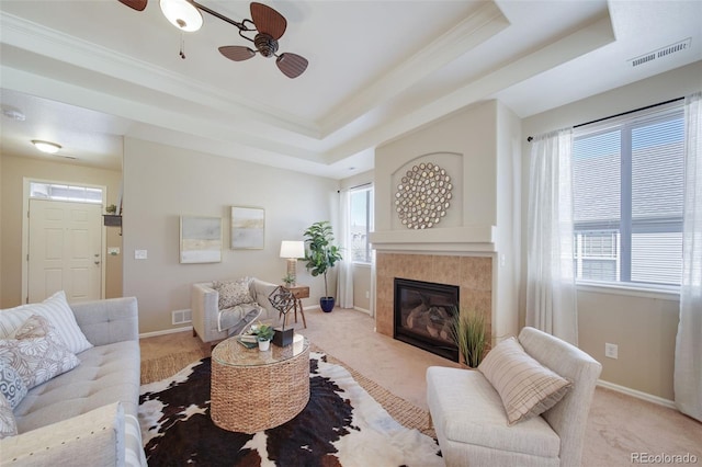living area featuring a tiled fireplace, light colored carpet, a tray ceiling, and visible vents