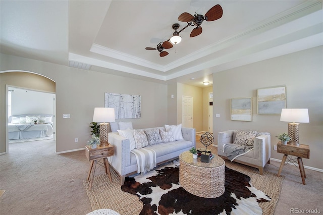 carpeted living area featuring a ceiling fan, visible vents, arched walkways, a raised ceiling, and ornamental molding