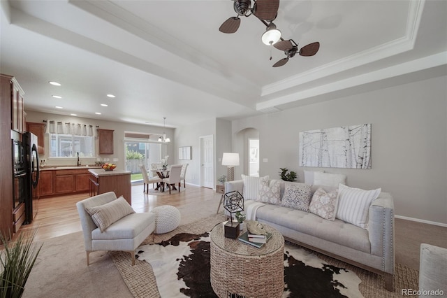 living area with ceiling fan, recessed lighting, light wood-type flooring, a tray ceiling, and arched walkways