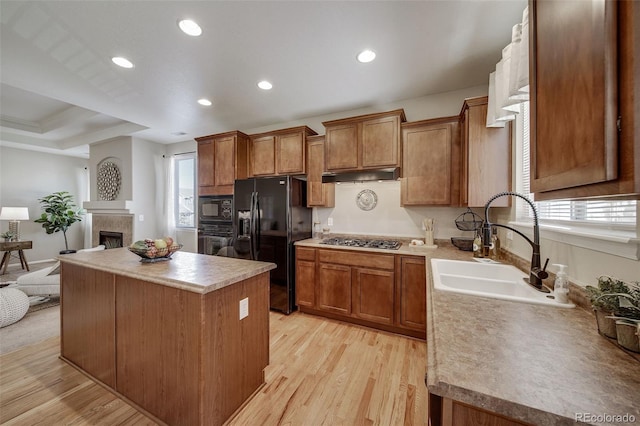 kitchen with under cabinet range hood, a healthy amount of sunlight, black appliances, and a center island
