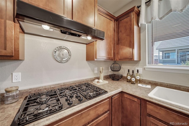 kitchen featuring light countertops, under cabinet range hood, brown cabinets, and black gas cooktop
