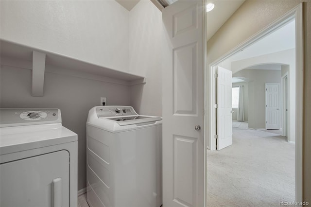 laundry room with separate washer and dryer, laundry area, light colored carpet, and arched walkways