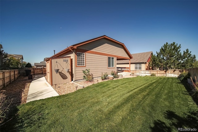 back of house with a lawn, a patio area, an outdoor structure, a fenced backyard, and a storage unit