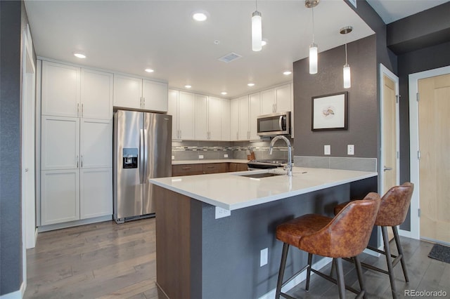 kitchen featuring visible vents, appliances with stainless steel finishes, a peninsula, wood finished floors, and a sink