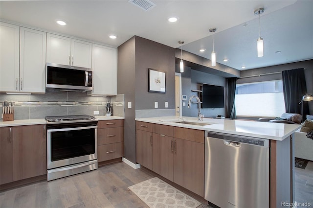 kitchen featuring visible vents, a peninsula, a sink, appliances with stainless steel finishes, and open floor plan