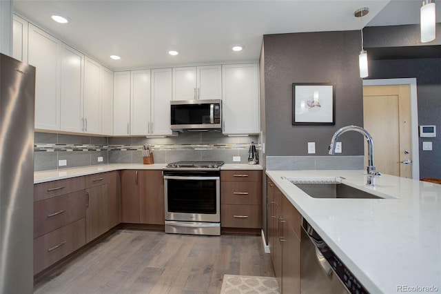 kitchen with backsplash, appliances with stainless steel finishes, wood finished floors, white cabinetry, and a sink