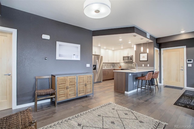 kitchen featuring a breakfast bar, wood finished floors, stainless steel appliances, a peninsula, and light countertops