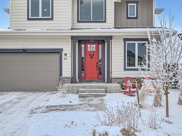 snow covered property entrance with a garage, stone siding, and board and batten siding