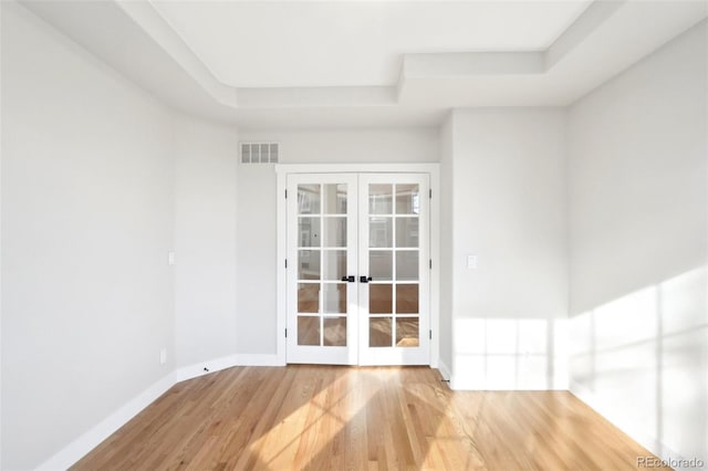 spare room featuring visible vents, a tray ceiling, wood finished floors, french doors, and baseboards