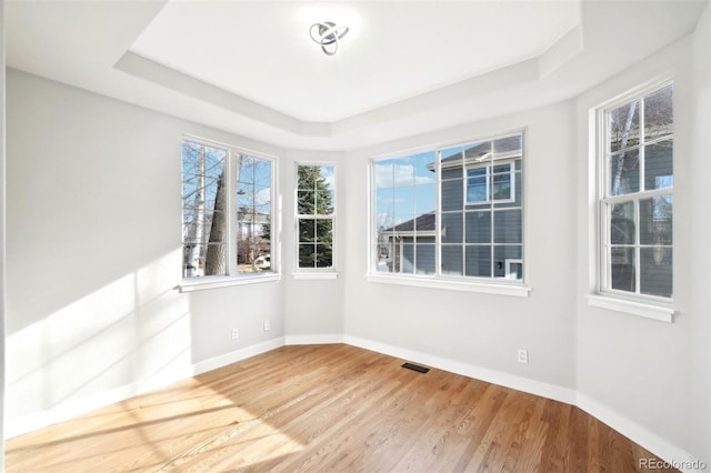 unfurnished room featuring a raised ceiling, wood finished floors, visible vents, and baseboards