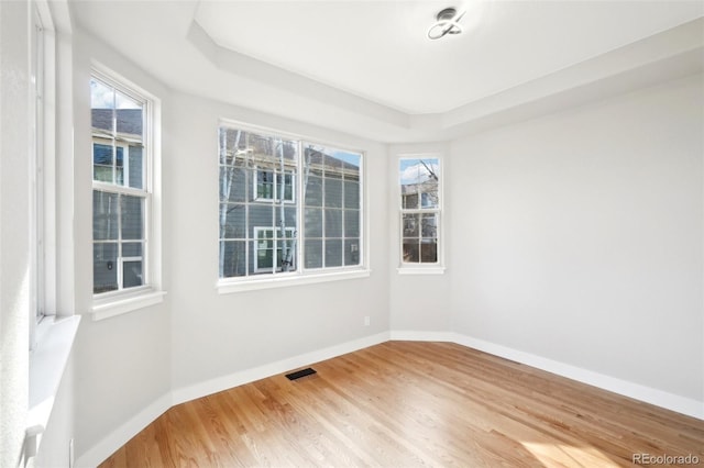 spare room featuring a tray ceiling, wood finished floors, visible vents, and baseboards