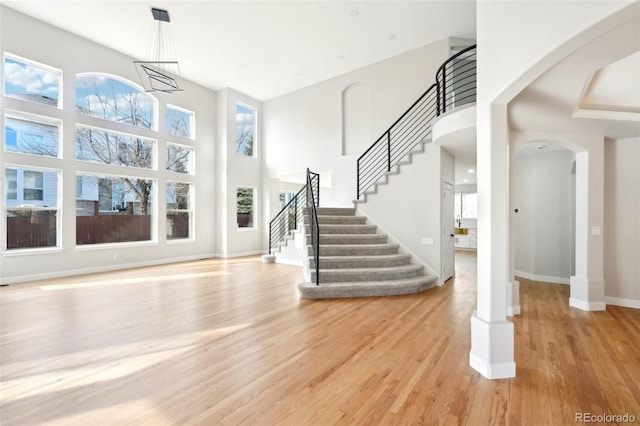 entrance foyer with light wood-style flooring, stairway, arched walkways, baseboards, and a towering ceiling