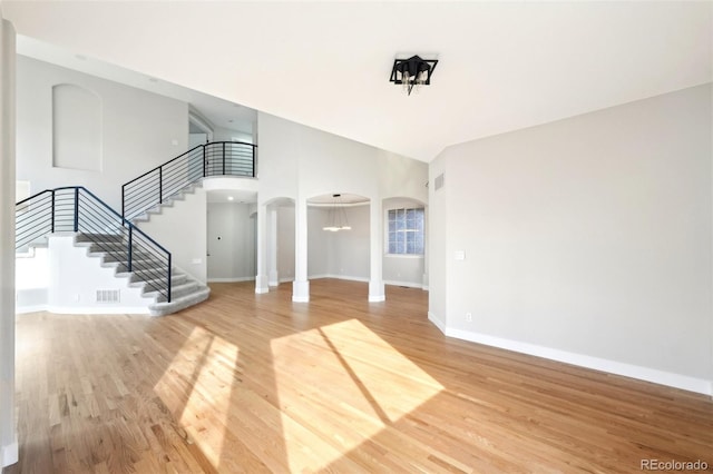 interior space featuring stairway, baseboards, a high ceiling, arched walkways, and light wood-style floors