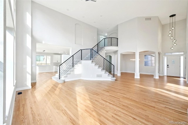 unfurnished living room featuring light wood finished floors, baseboards, stairs, a high ceiling, and arched walkways