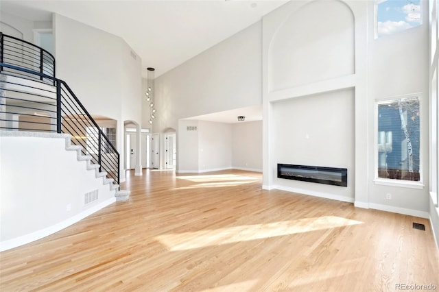 unfurnished living room with a glass covered fireplace, stairway, a high ceiling, and visible vents