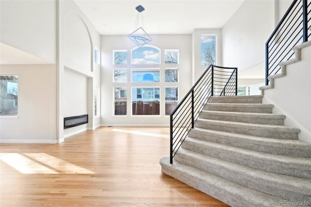 stairs with a glass covered fireplace, a high ceiling, wood finished floors, and baseboards