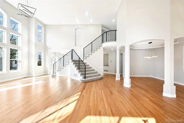 unfurnished living room featuring light wood-type flooring, arched walkways, a high ceiling, baseboards, and stairs