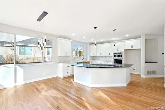 kitchen with visible vents, backsplash, light wood-style floors, hanging light fixtures, and white cabinetry