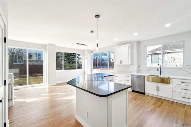 kitchen with a sink, light wood-style floors, dishwasher, tasteful backsplash, and a center island