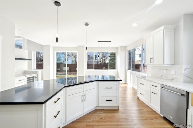 kitchen featuring light wood finished floors, white cabinets, stainless steel dishwasher, decorative light fixtures, and backsplash