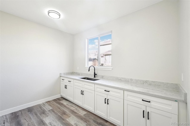 kitchen featuring baseboards, light stone countertops, light wood-style flooring, white cabinetry, and a sink