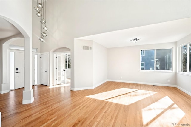 interior space featuring visible vents, baseboards, light wood-style flooring, a high ceiling, and arched walkways