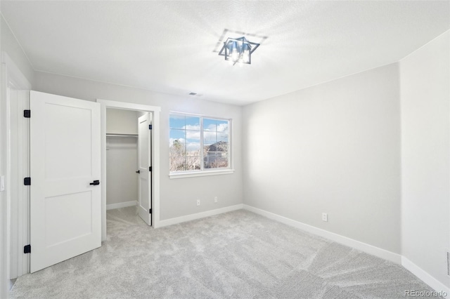 unfurnished bedroom with a spacious closet, light colored carpet, a closet, and baseboards