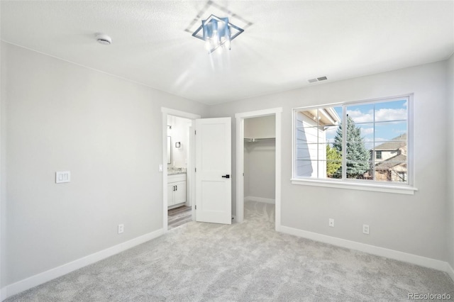 unfurnished bedroom featuring baseboards, light carpet, visible vents, and a walk in closet