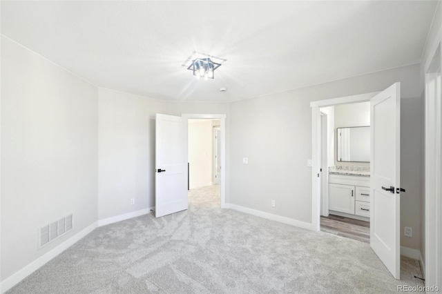 unfurnished bedroom featuring visible vents, baseboards, light colored carpet, and ensuite bathroom