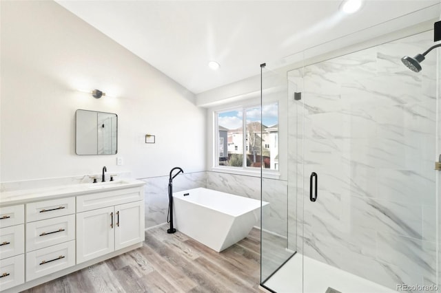 bathroom with vanity, wood finished floors, a marble finish shower, lofted ceiling, and a freestanding bath