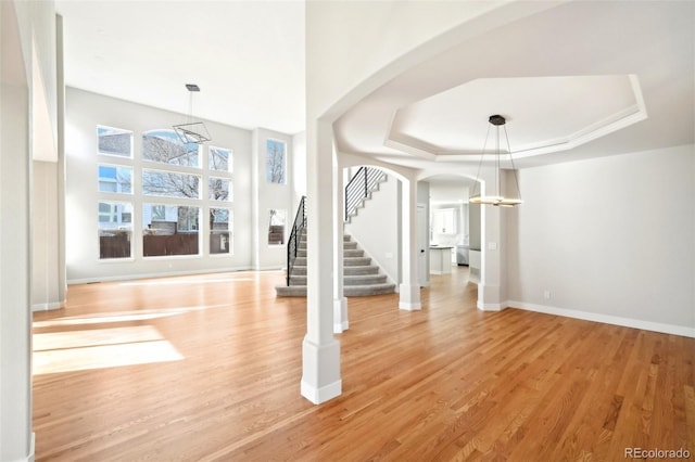 entryway with arched walkways, light wood-style flooring, stairs, and a raised ceiling