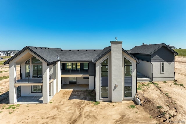 rear view of property featuring a chimney, stucco siding, a patio, and roof with shingles