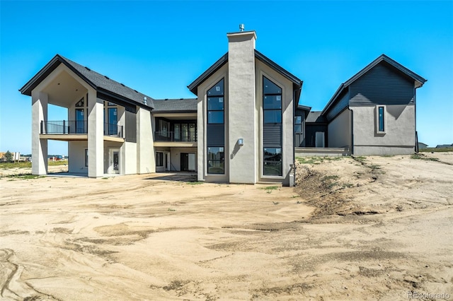 rear view of property with a chimney, stucco siding, and a balcony