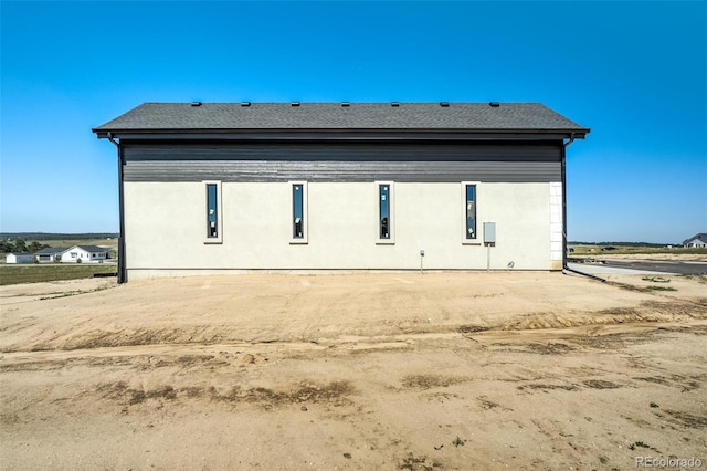 rear view of house with stucco siding and a shingled roof