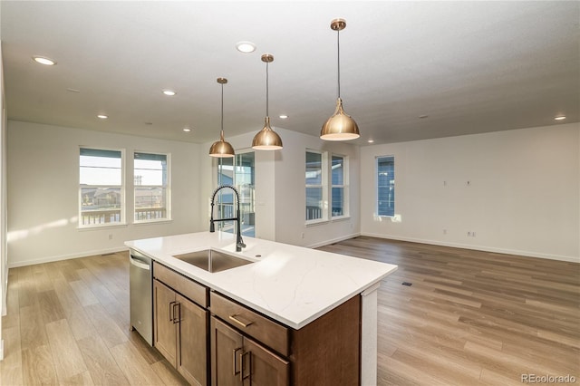 kitchen with light wood-type flooring, decorative light fixtures, light stone countertops, sink, and an island with sink