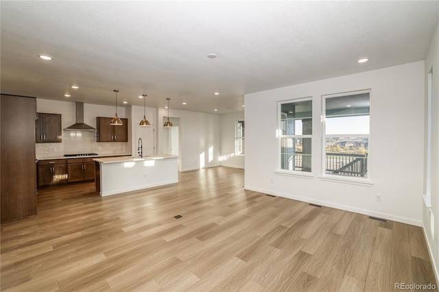 unfurnished living room with a textured ceiling, sink, and light hardwood / wood-style flooring