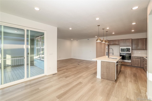 kitchen with light hardwood / wood-style flooring, appliances with stainless steel finishes, an island with sink, and hanging light fixtures